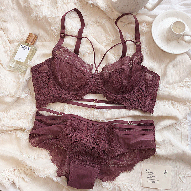 Women's lace gathered bra and matching underwear set in wine red color with intricate lace detailing and adjustable straps, styled on a soft fabric background with a perfume bottle and a cup.