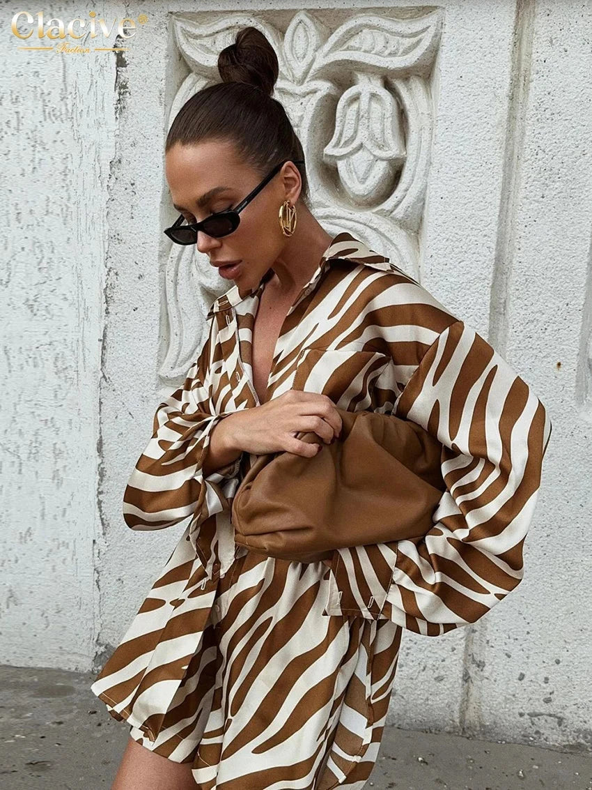 woman wearing elegant stripe print 2-piece outfit with long sleeve shirt and high-waisted shorts holding brown clutch