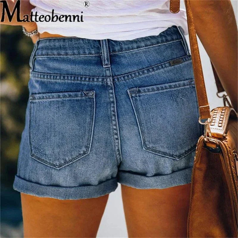 Back view of high waisted ripped denim shorts for women with rolled hem and pockets, styled with a white top and brown leather bag.