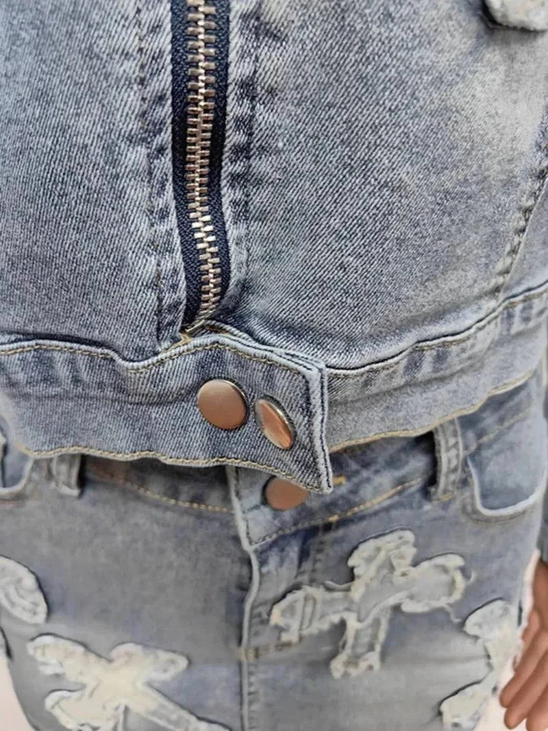 Close-up of chic denim tassel two-piece set featuring zipper, buttons, and embroidered cross details on faded blue denim fabric