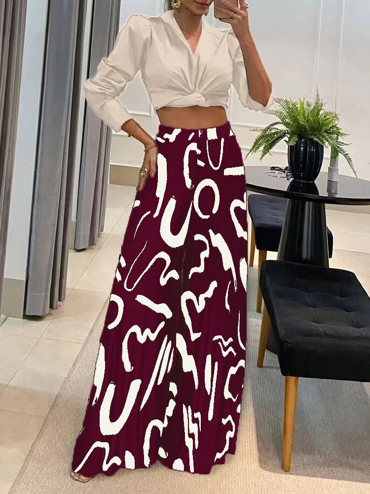 Woman wearing geometric print wide leg pants with abstract white shapes on dark maroon background and white cropped blouse indoors