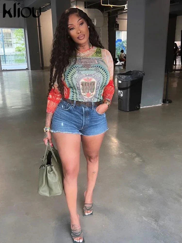woman wearing Kliou Dollar Print long sleeve mesh top with colorful dollar design paired with denim shorts and green handbag in indoor setting