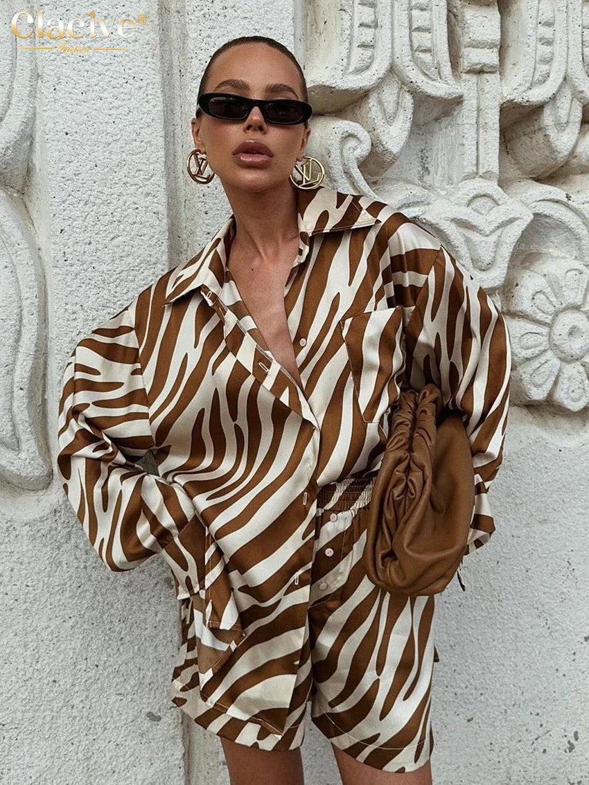 woman wearing elegant stripe print long sleeve shirt and shorts set with sunglasses and brown clutch bag near textured wall