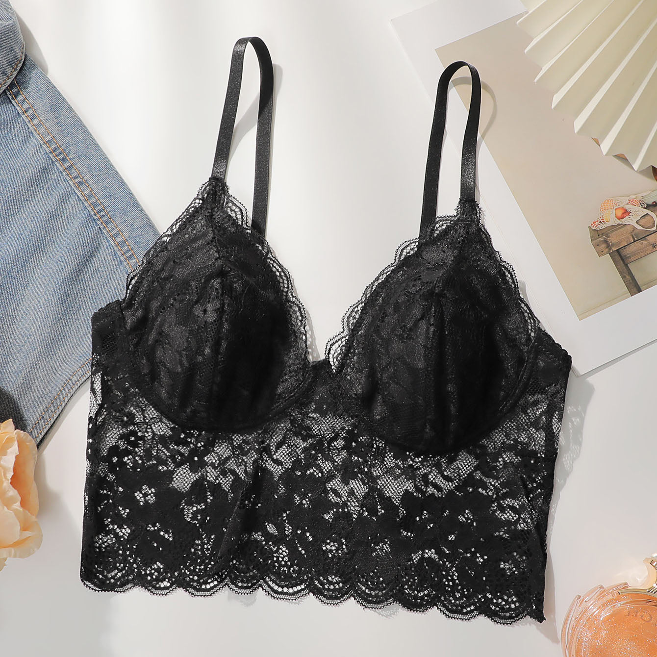 Black elegant floral lace bodycon bra with scallop trim and adjustable straps on white background with denim and decorative items