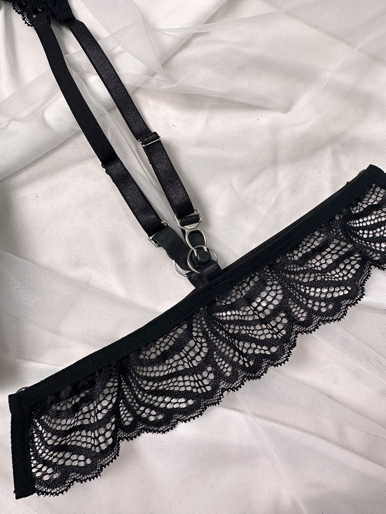 Black lace lingerie strap with steel ring and adjustable buckle on white fabric background