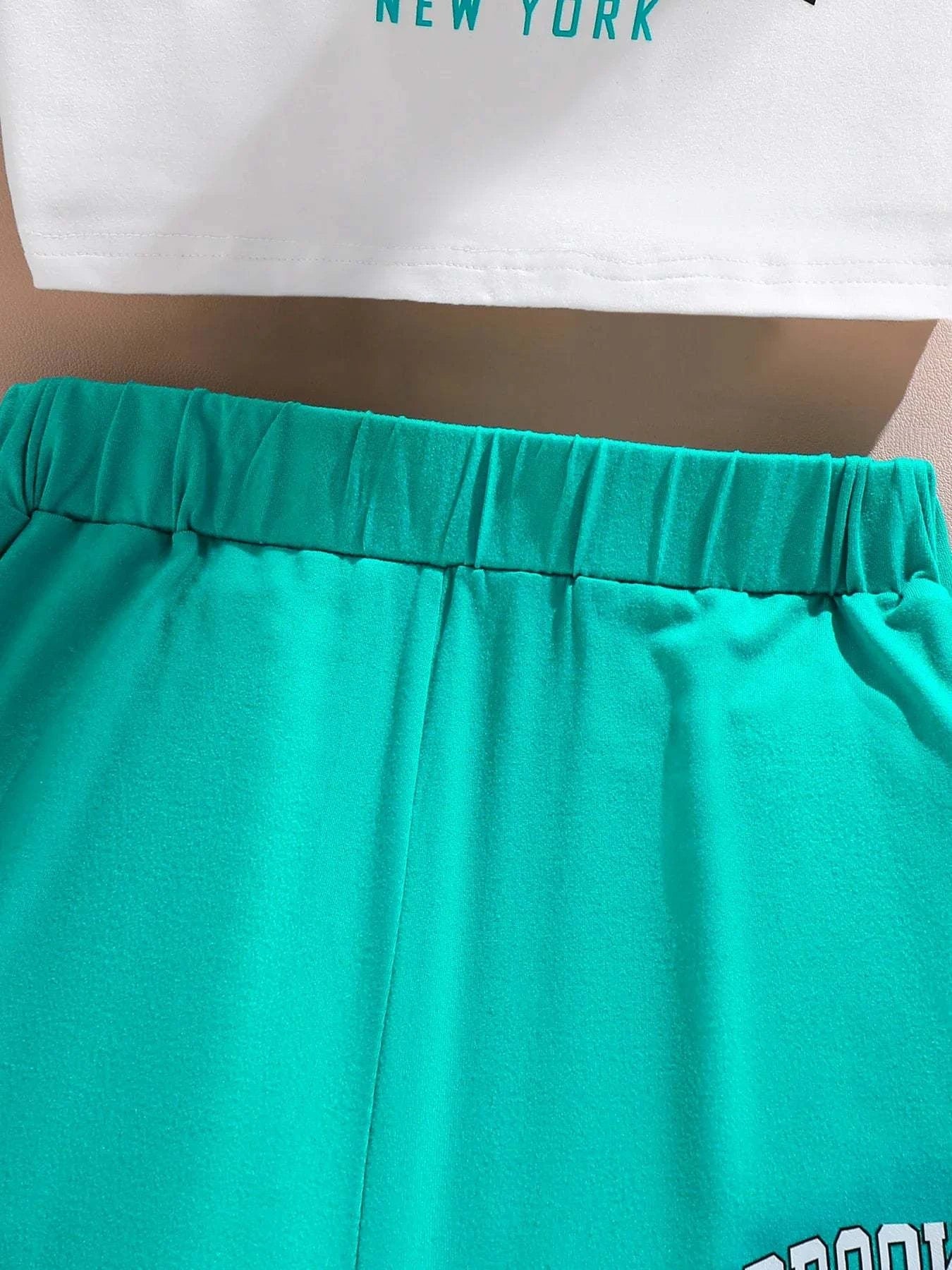 Close-up of bright turquoise elastic waist shorts from girls' trendy 3-piece summer outfit set with white top hem visible above.