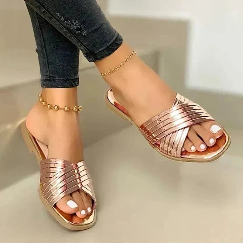 rose gold women's fashion flip-flops with crisscross strap design and cushioned sole worn with black jeans and ankle bracelets