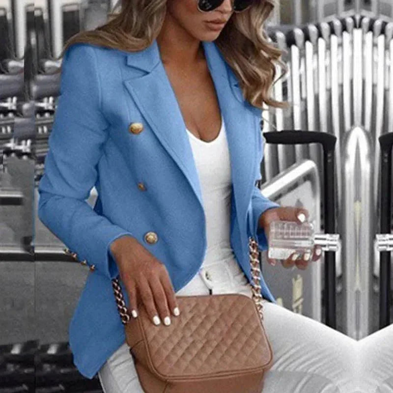 Woman wearing a stylish light blue customizable women's blazer suit with gold buttons, paired with white top and pants, holding a quilted brown purse.