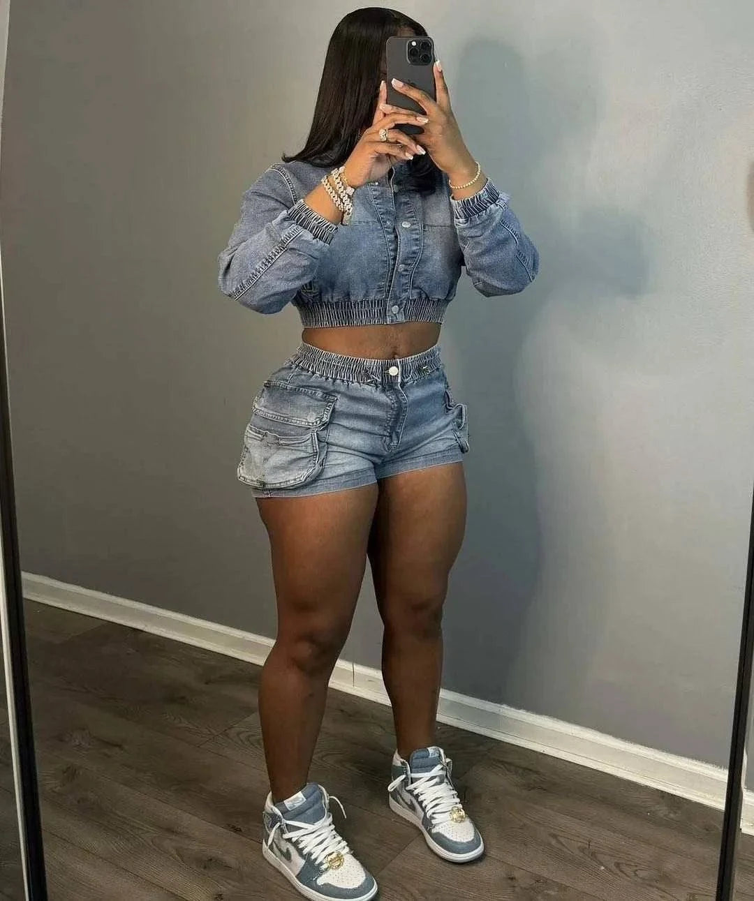 Woman wearing chic multi pocket denim shorts set with matching cropped jacket and sneakers taking mirror selfie