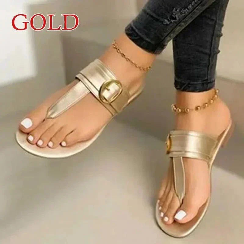 Gold women's fashion flip-flops with ankle chain and buckle detail, worn with dark jeans.