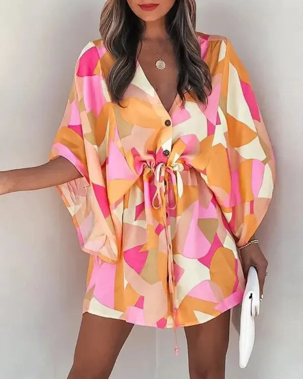 Woman wearing colorful fashion print V-neck lace-up summer dress with pink, orange, and white patterns, holding a white clutch.