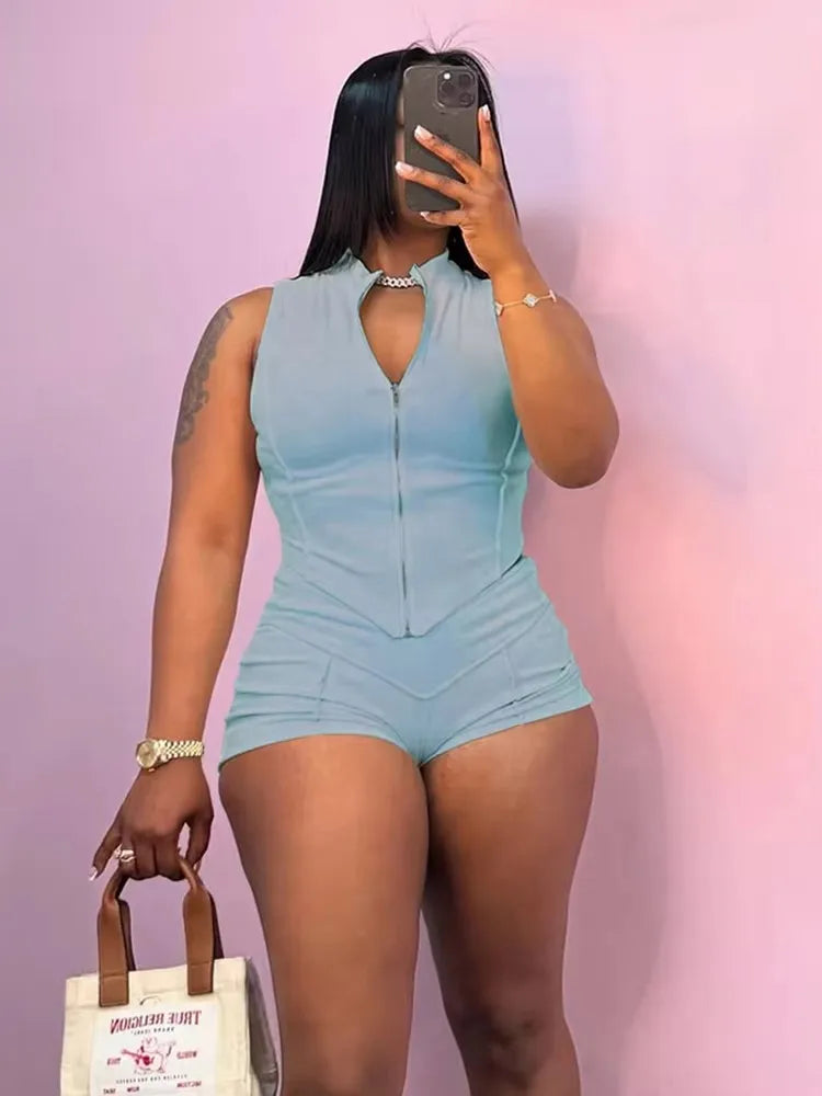 woman wearing sporty chic patchwork light blue zip-up sleeveless crop top and matching shorts set holding beige handbag against pink background