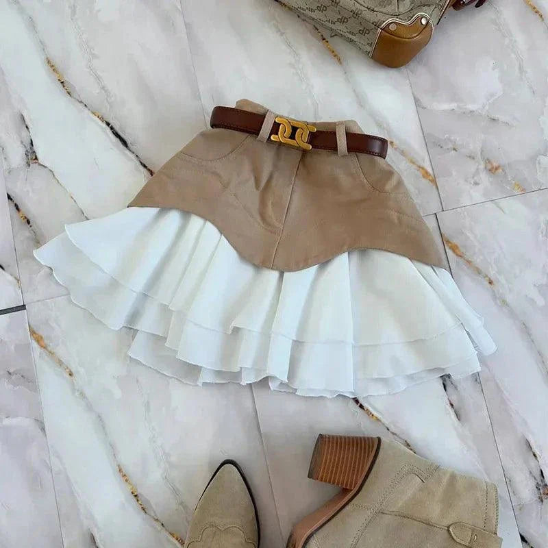 High waist ruffle edge denim skirt with layered white ruffle hem and brown belt on marble floor with beige boots and handbag.