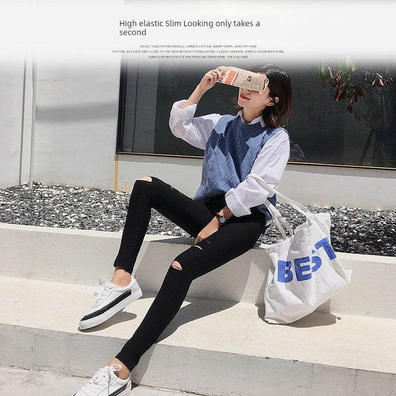 Woman wearing black ripped leggings and white sneakers sitting outdoors with a tote bag, casual spring and fall fashion.