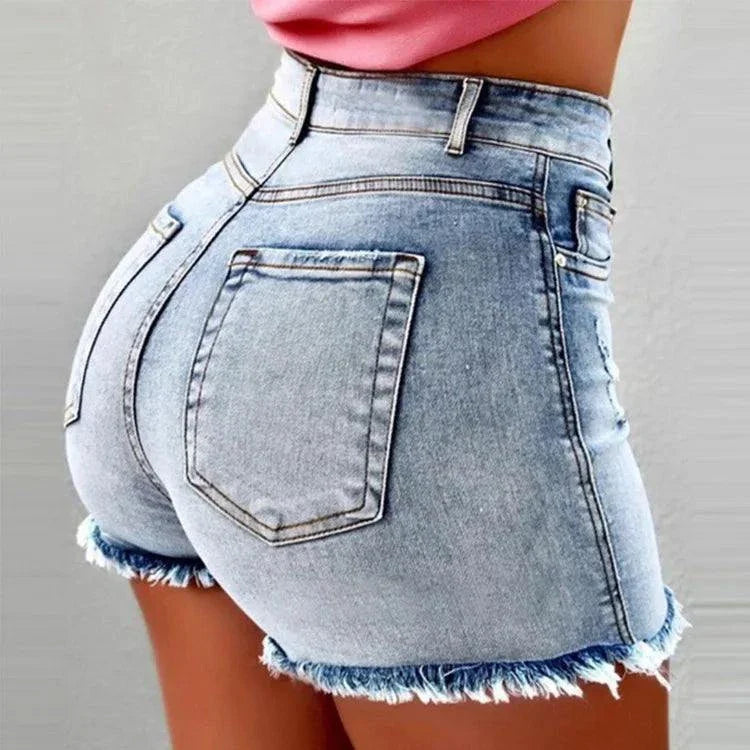 Close-up of vintage distressed denim shorts with frayed hems and a washed finish on a woman wearing a pink top