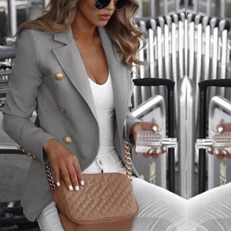 Stylish gray customizable women's blazer suit with gold buttons worn with white top and pants, accessorized with quilted brown handbag and sunglasses.