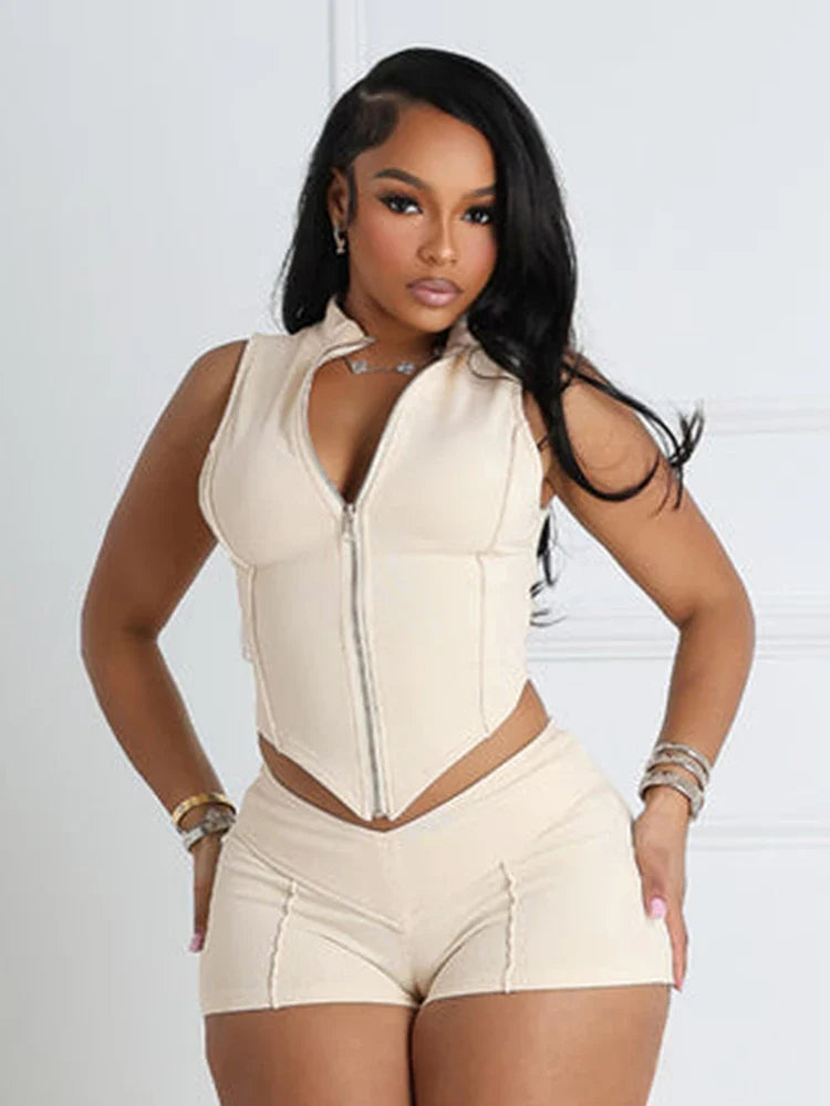 woman wearing beige sporty chic patchwork sleeveless zip-up crop top and matching shorts set against white background