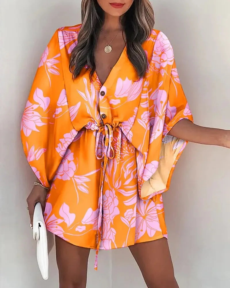 Woman wearing orange and pink floral fashion print V-neck lace-up summer dress with loose sleeves and drawstring waist.