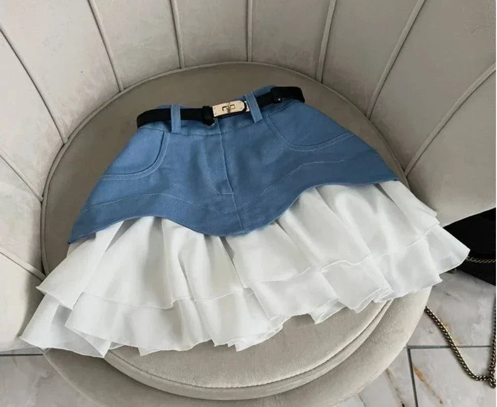 High waist ruffle edge denim skirt with layered white frill hem and black belt detail on a beige chair.