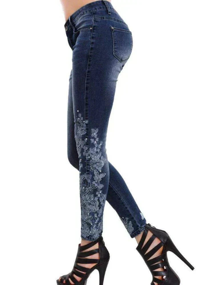 Women's dark blue skinny jeans with floral embroidery on the lower leg paired with black high-heeled sandals