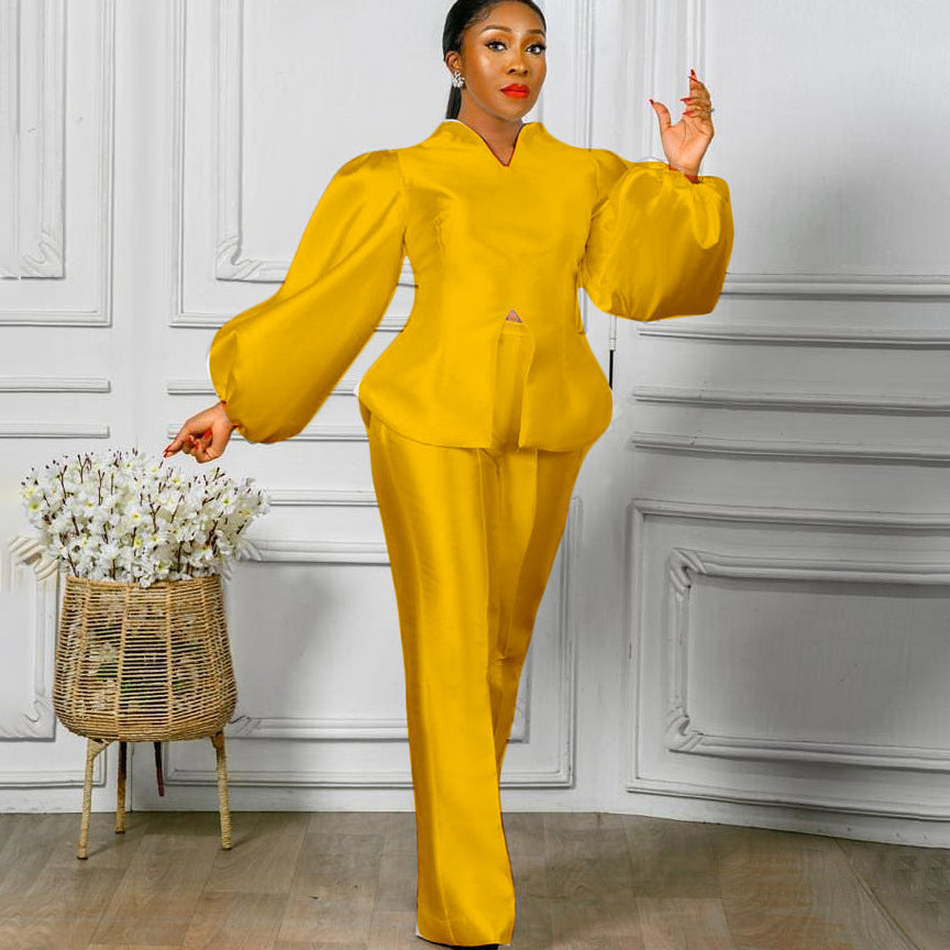 Woman wearing yellow women's fashion solid color puff sleeve top with wide leg pants standing indoors next to a floral arrangement