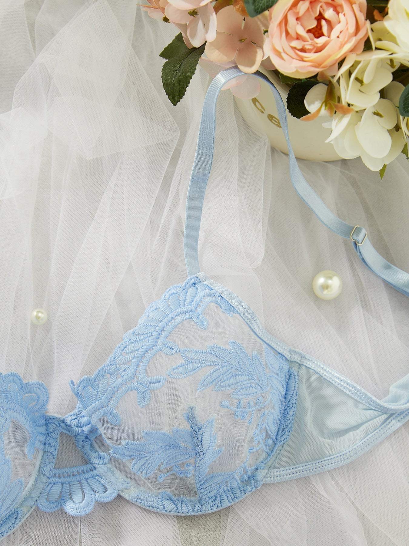 Light blue embroidered mesh lace push-up bra with floral design and adjustable strap on sheer fabric background with flowers and pearls.