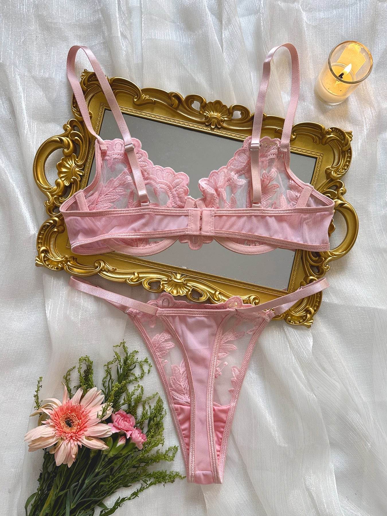 Pink women's embroidered mesh lace push-up lingerie set with bra and thong on gold ornate mirror with flowers and candle on