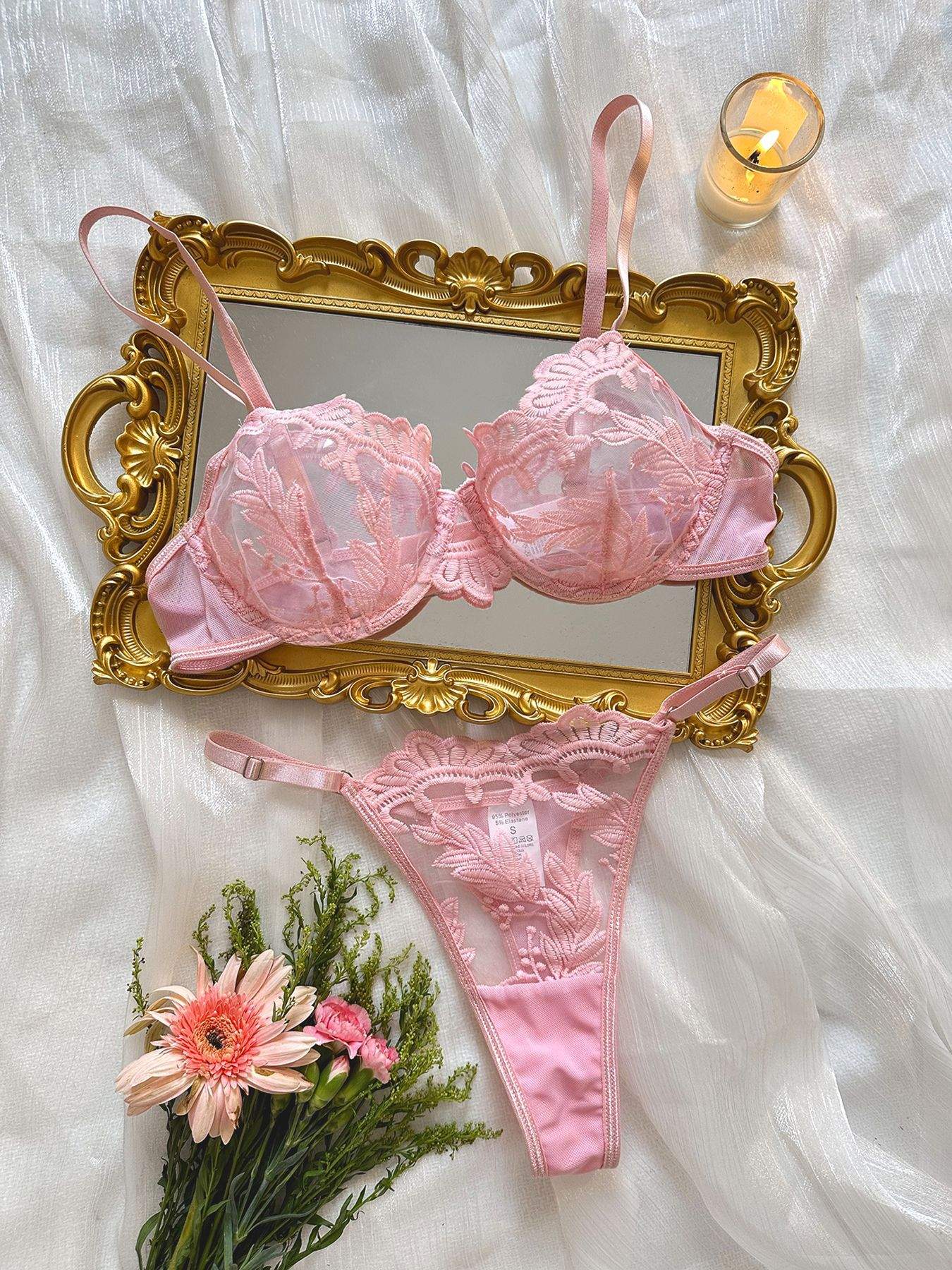 Pink women's embroidered mesh lace push-up lingerie set on decorative gold frame with flowers and candle background